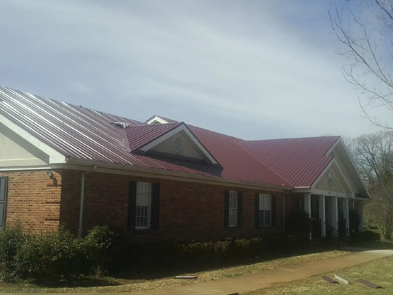 Red metal roof with gabled entries on a long brick building, from a Hail Damage Roof Repair job in Mooreland