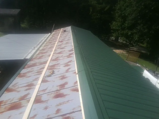 Old rusted panels beside newly installed green metal roofing — Wind Damage Roof Repair by Roofing Brothers in Mooreland