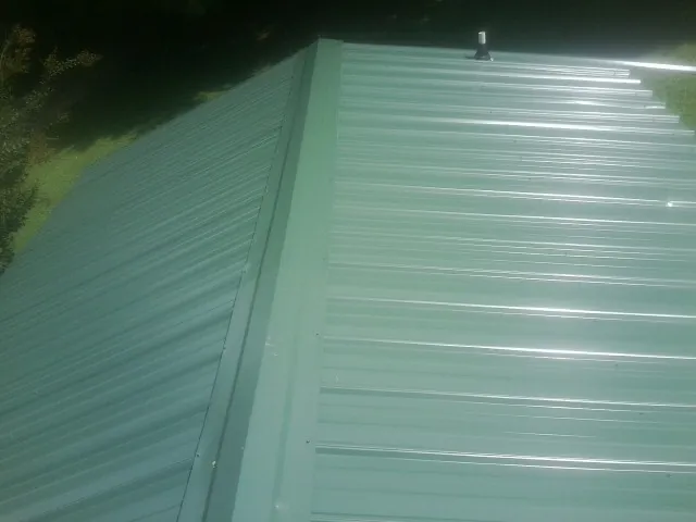 New green metal panels meeting at the ridge of a roof — Flat Roof Repair work by our crew in Mooreland
