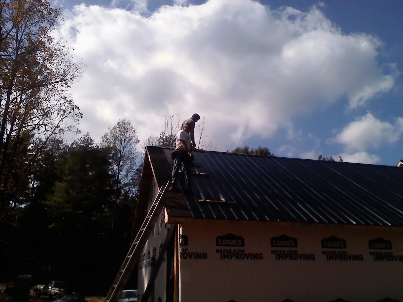Roofer fastening dark metal panels high against a cloudy sky, from a Roof Inspection job in Mooreland