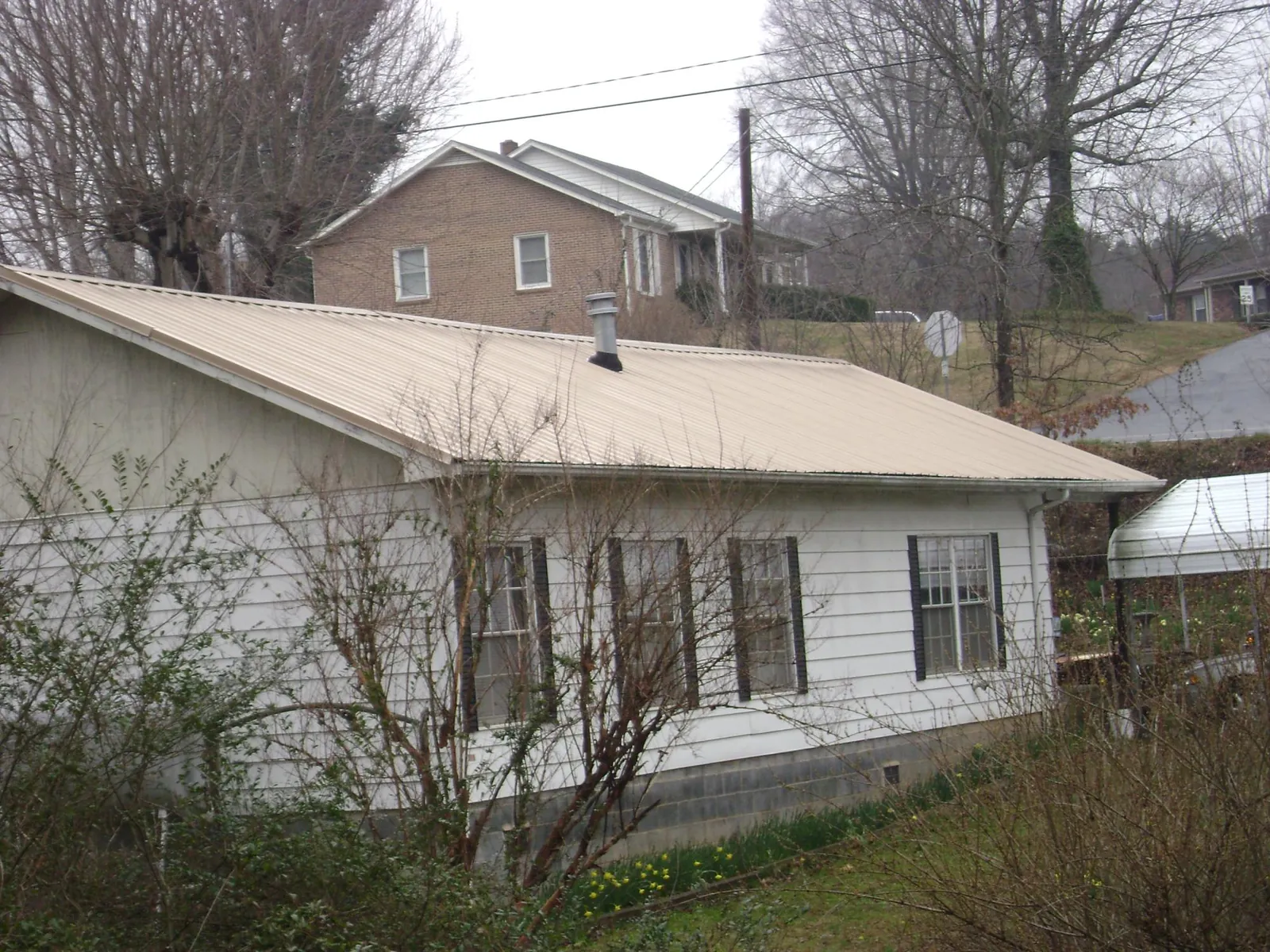 Tan metal roof on a white sided house set into a hillside — Commercial Roofing by Roofing Brothers in Mooreland