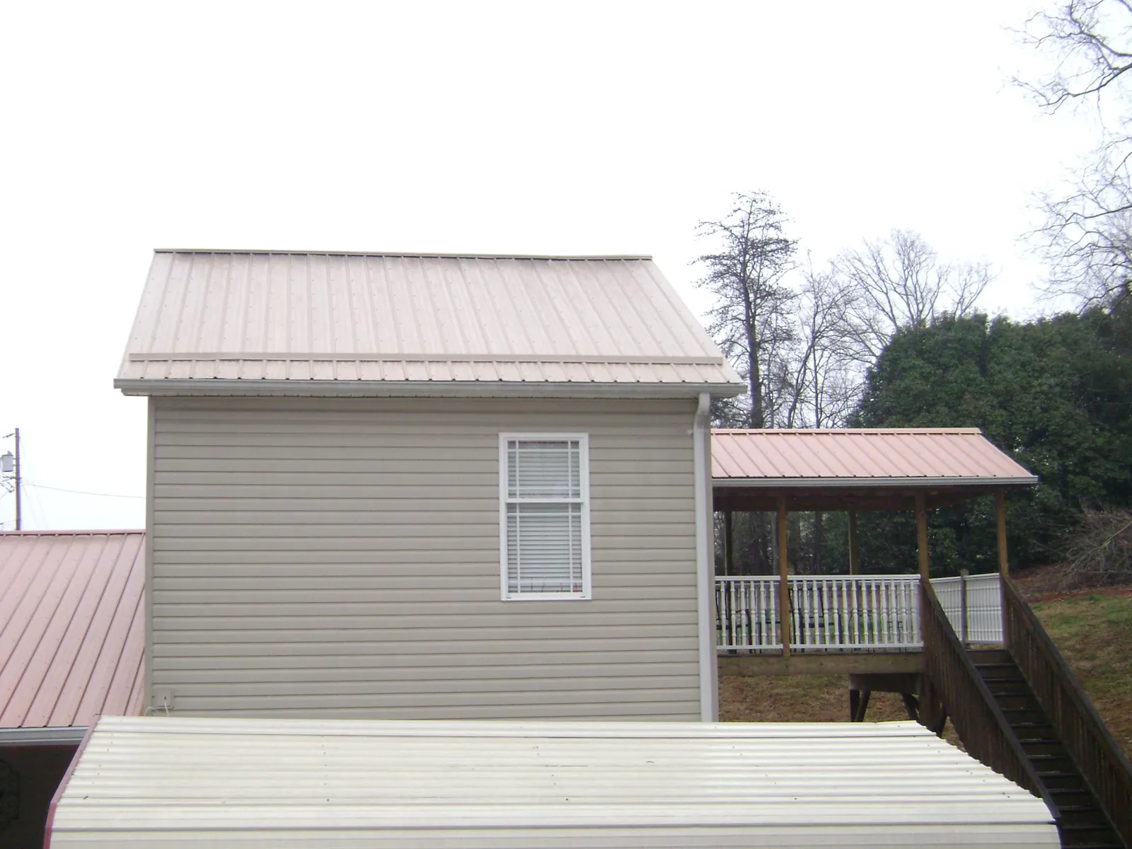Tan metal roofs on a two story addition and attached porch, from a Roof Replacement job in Mooreland